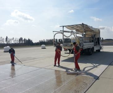 Several employees in work clothes priming a floor with a transporter in the background